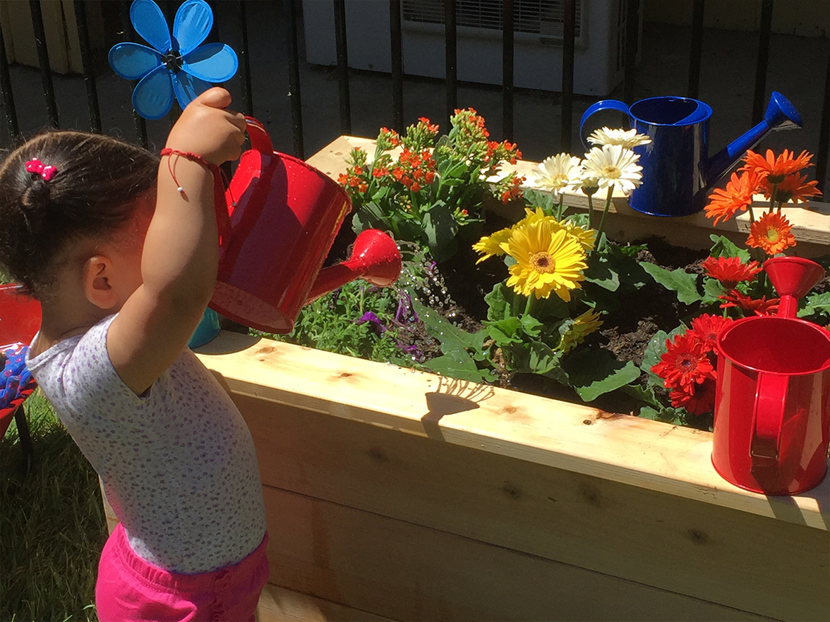 A young girl thoughtfully waters flowers in a raised garden